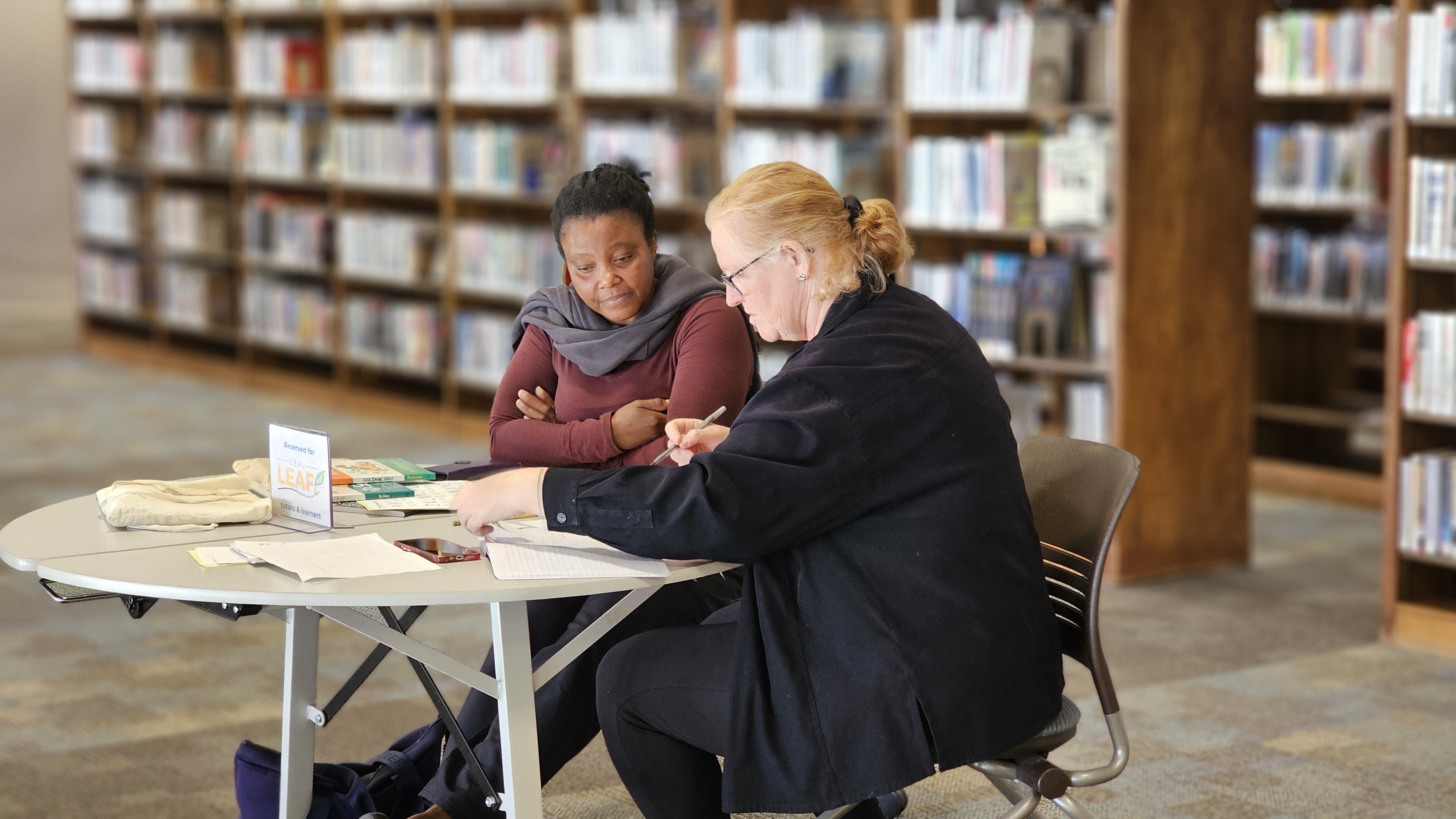 tutor sitting at table with learner at the library