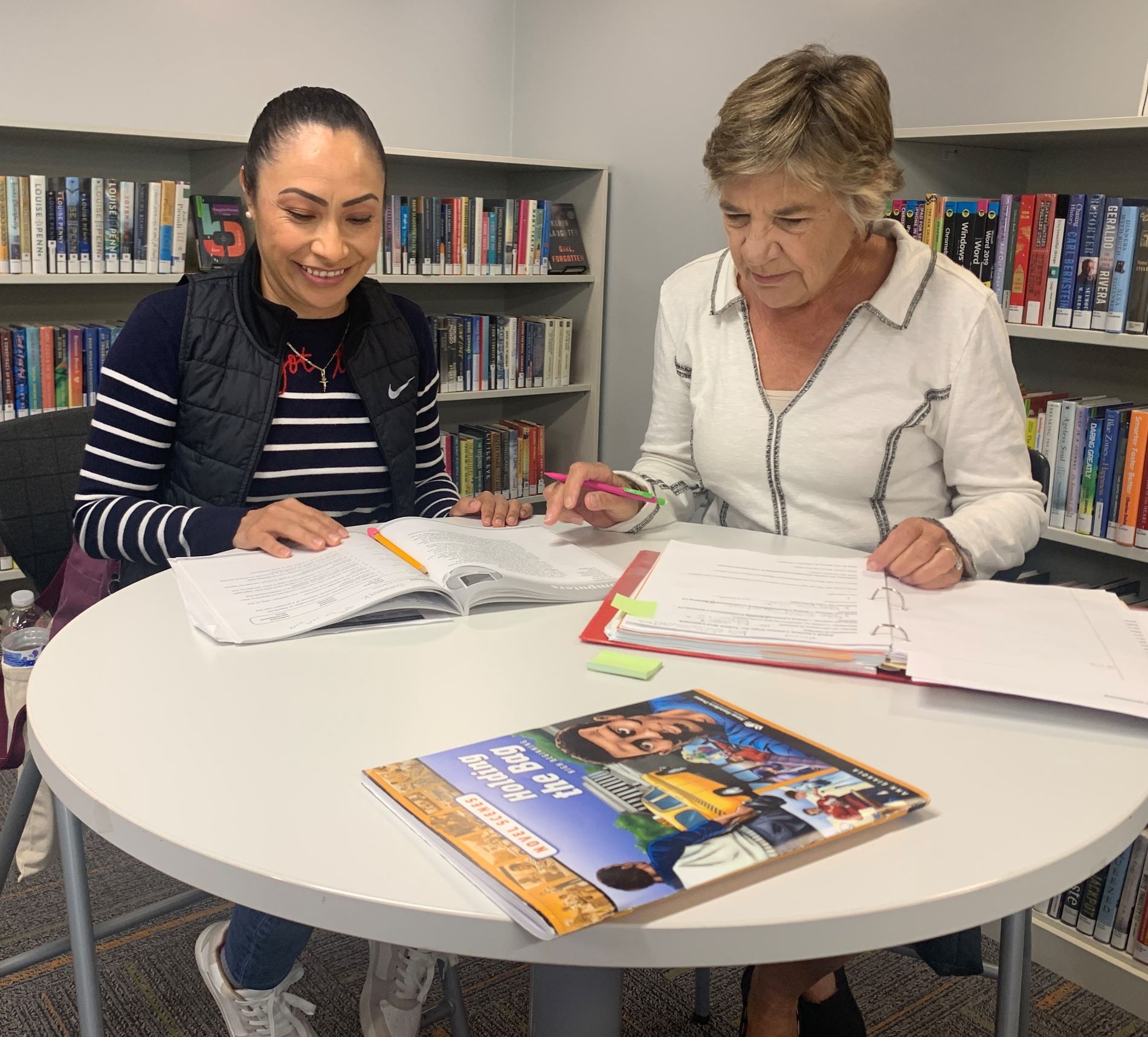 A female tutor and a female learner are sitting at a table looking over a book together.