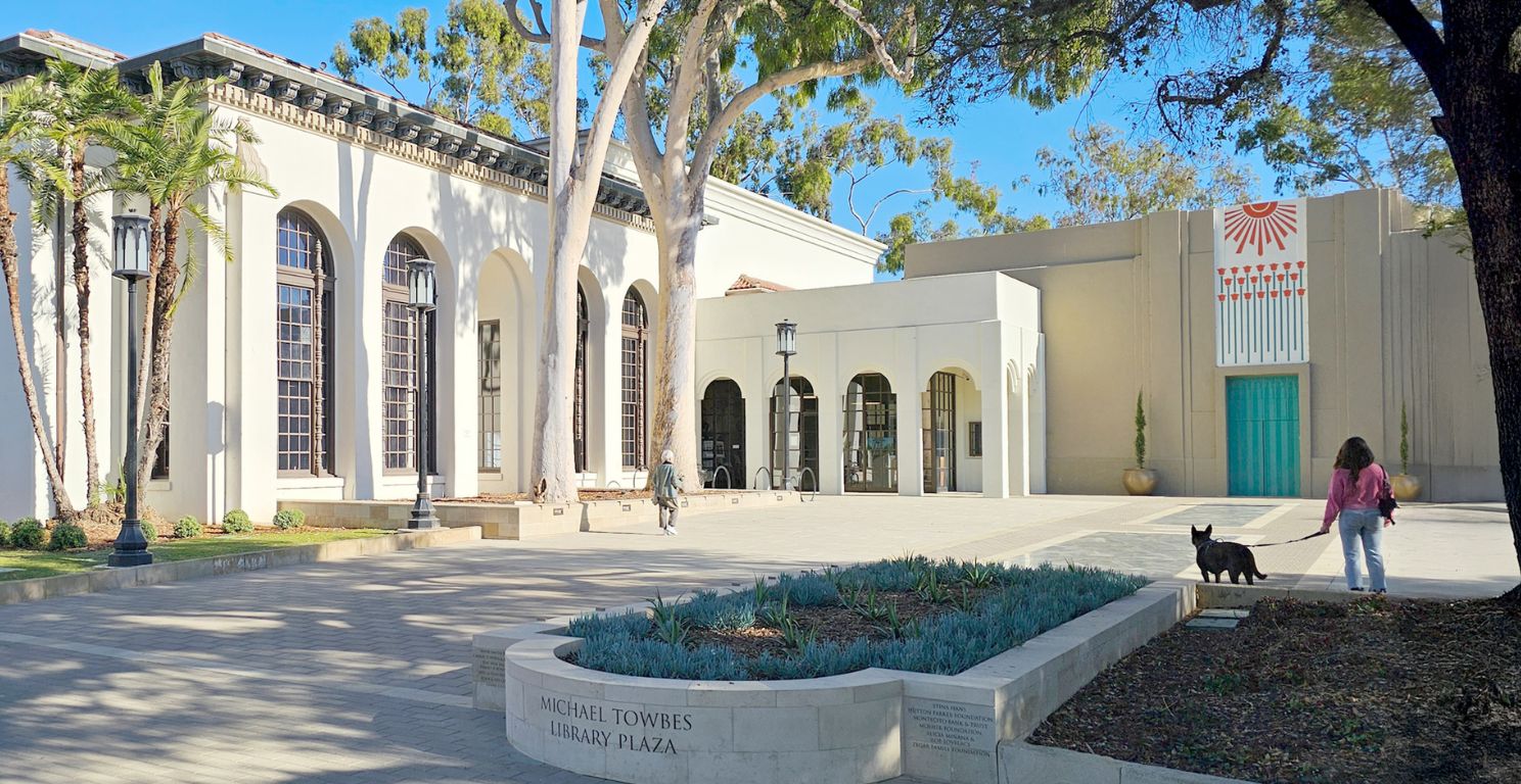a person and their dog stand outside the Central Library building in a large open plaza space