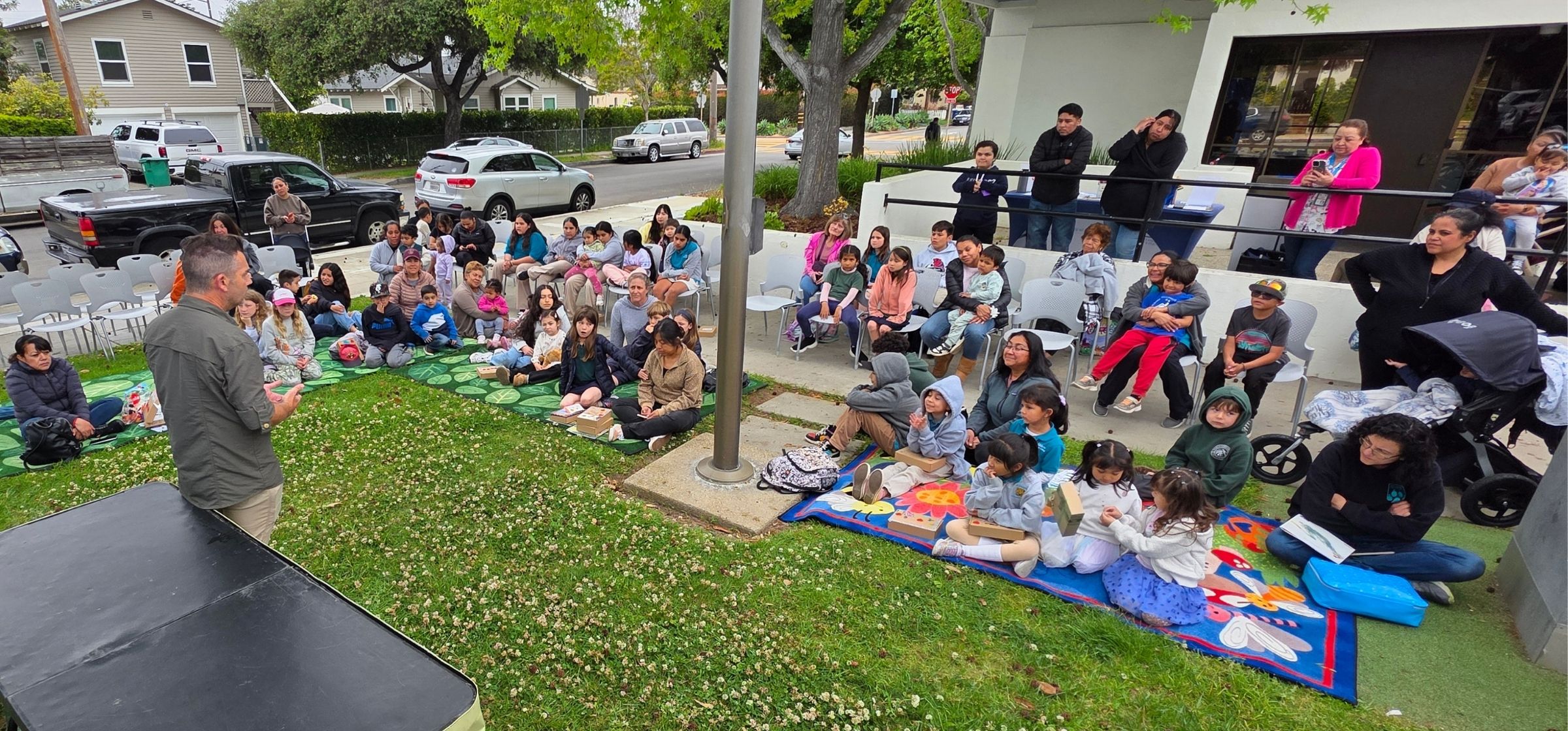 Children sit on the front lawn of the Eastside Branch for Dia de los ninos
