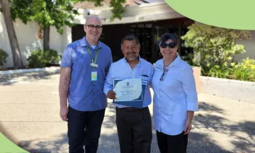 high school graduate holds diploma with mother and library staff member on each side