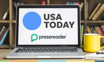 laptop open to USA today on a table with a yellow mug of coffee