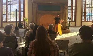 A patron reads poetry to a seated crowd in the library