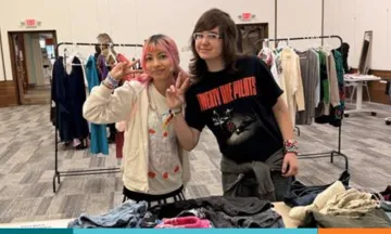 Two teens waving to camera holding clothing