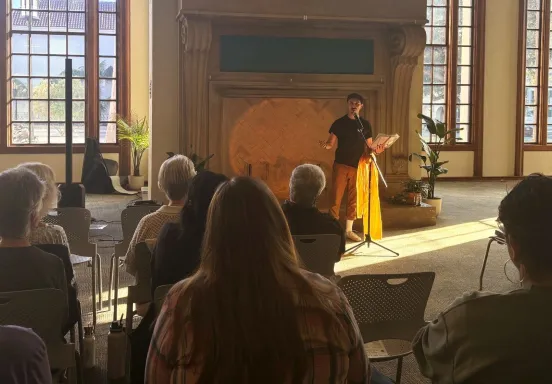 A patron reads poetry to a seated crowd in the library