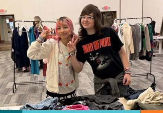 Two teens waving to camera holding clothing