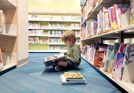 child reads a book in a library aisle