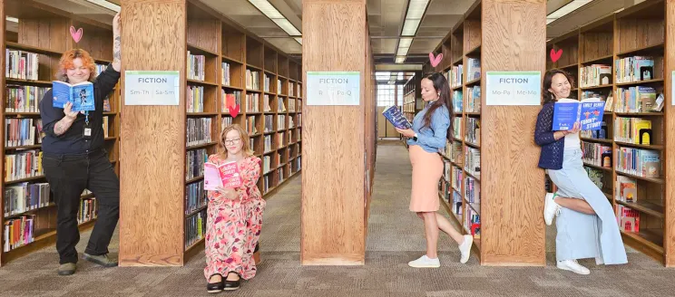 four library staff members read books in between the stacks