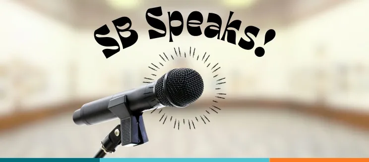 A microphone on a stand in the foreground with the text “SB Speaks!” above on a transparent room background.