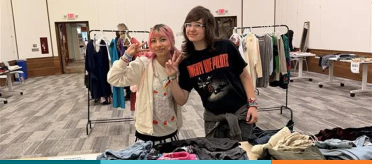 Two teens waving to camera holding clothing
