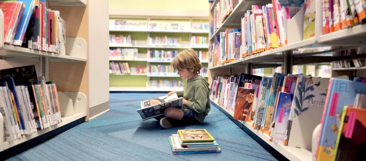 child reads a book in a library aisle