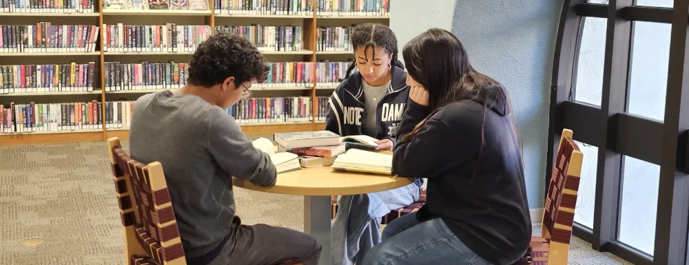 three teens sitting at a round table in the teen area at central library