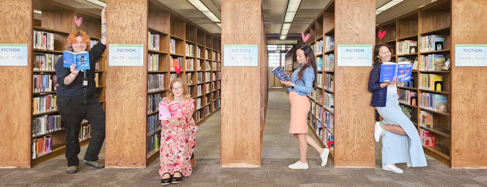 four library staff members read books in between the stacks