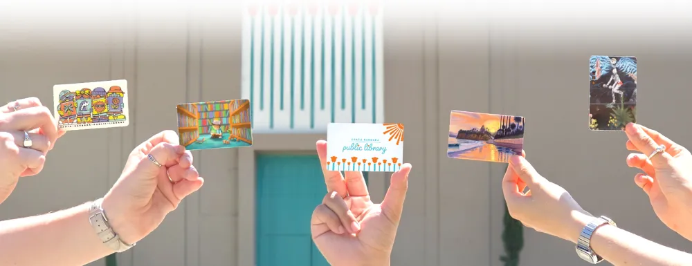 Hands holding library cards in front of the Sunburst Over California Poppies mural.