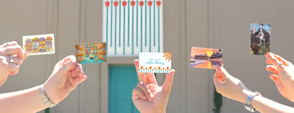 Hands holding library cards in front of the Sunburst Over California Poppies mural